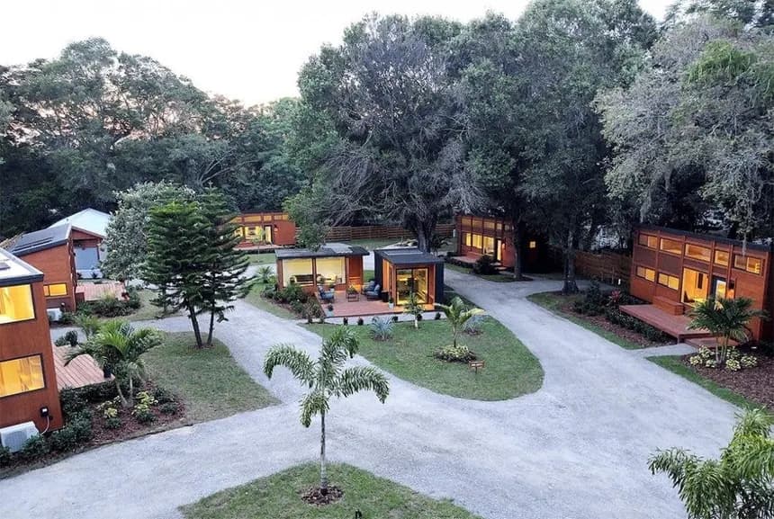 Modern Escape tiny homes along a gravel path through landscaped lawns at dusk, warmly lit interiors and wooden decks.
