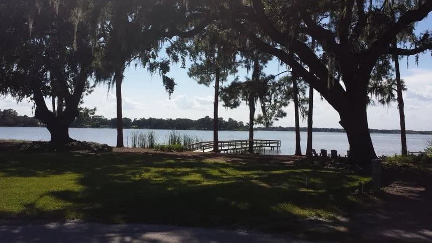 Shaded lakeside grassy area with moss-draped oaks framing a dock extending onto calm water at Lake Mariana.