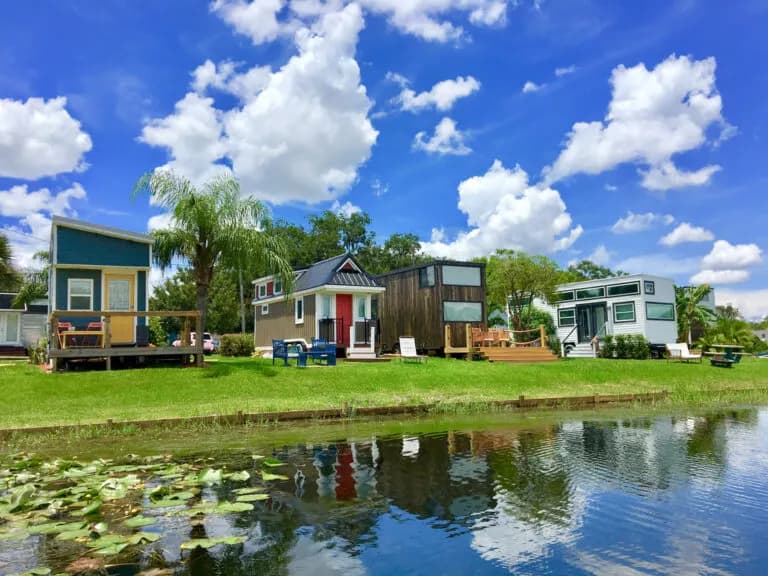 Colorful lakeside tiny homes at Tiny Town Orlando on Lake Fairview, with grass and reflections on the water.